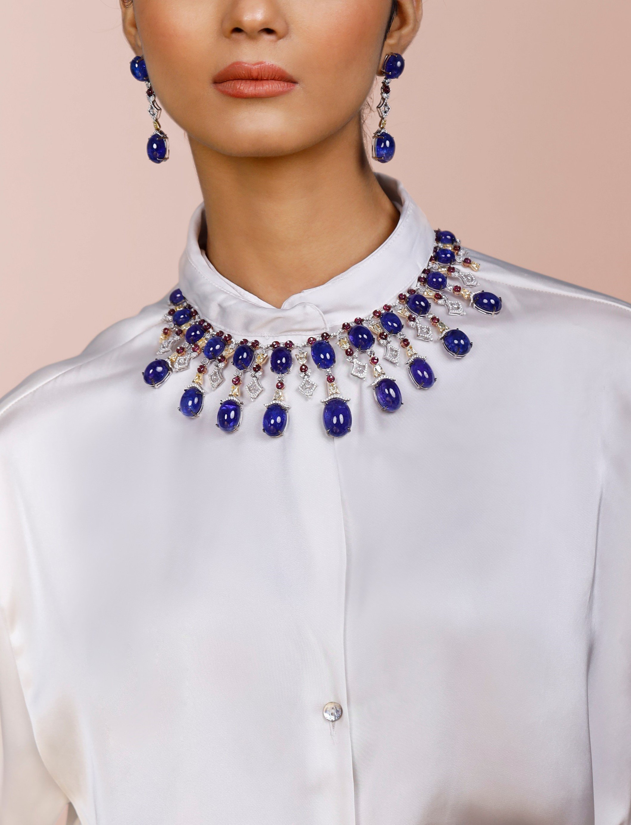 A tanzanite cabochon, ruby and diamond necklace with matching drop earrings, worn with a white silk shirt